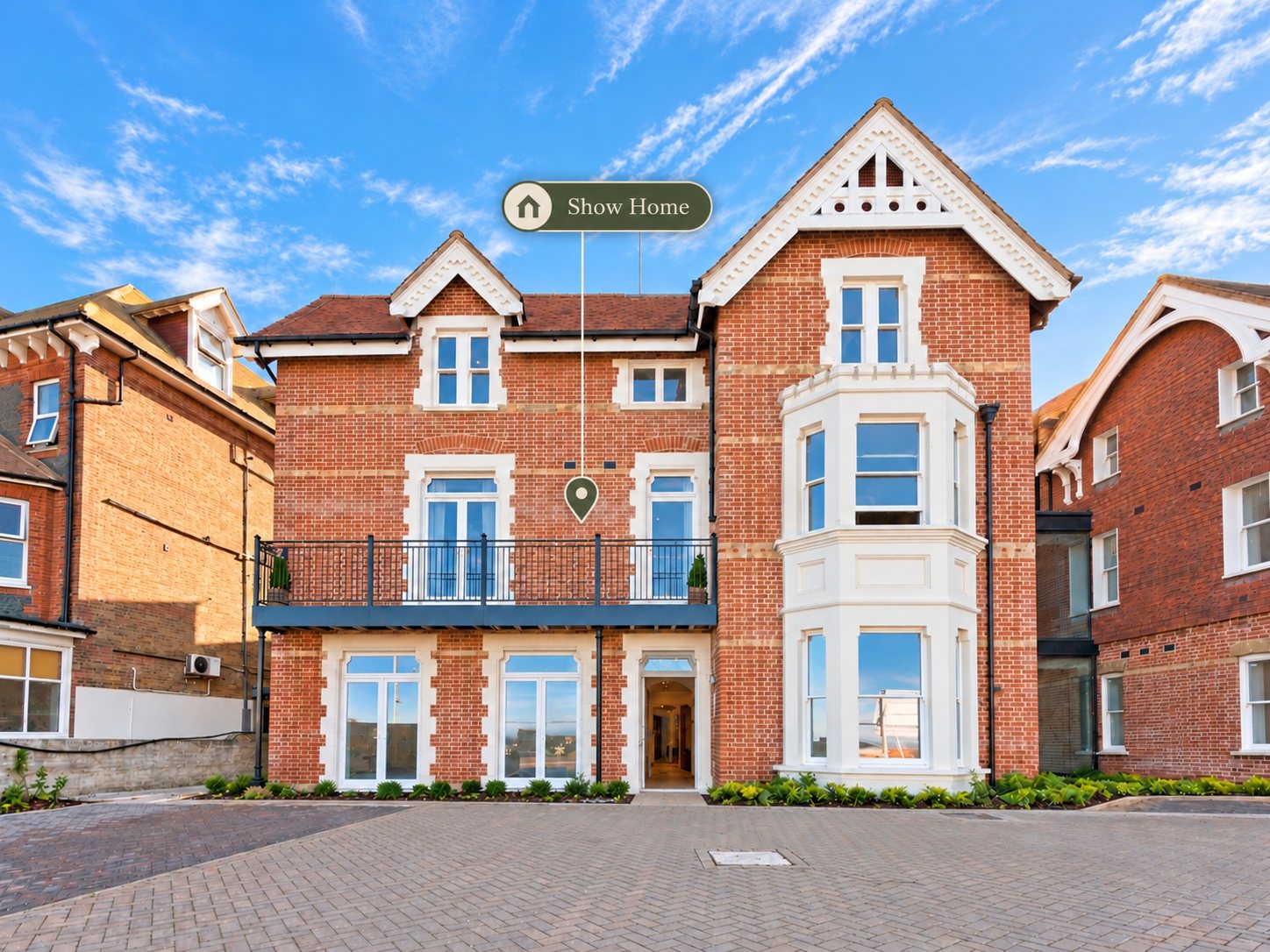 Front elevation of one of the Chalk House villas: red brick, white bay windows, a first floor balcony and a decorative gable
