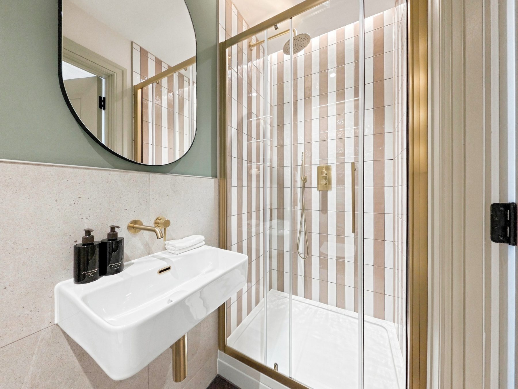 Shower room with striped wall tiling, brushed brass fittings and a wall hung basin