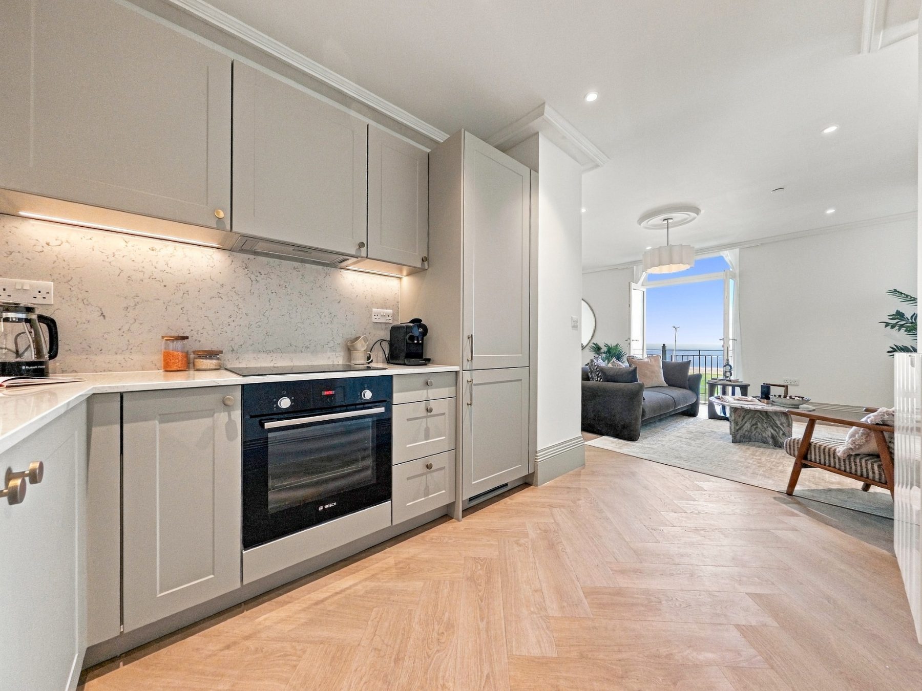 Shaker style kitchen in soft grey with integrated oven and a view through to the living area